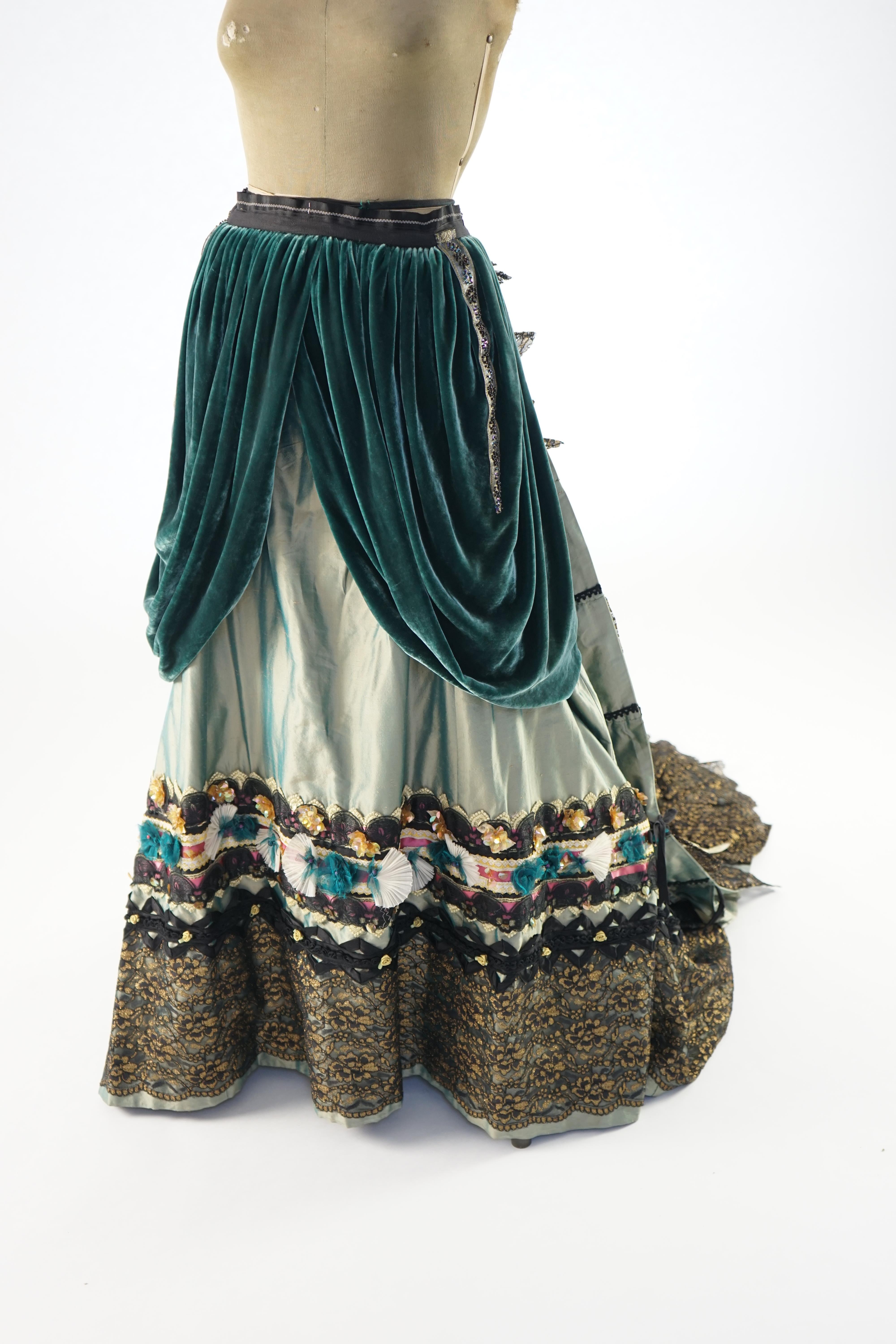 An Edwardian style lady's green taffeta skirt decorated with beaded, sequinned, ribboned border and swags of silk velvet, together with matching train layered with frilled black and gold lace, appliquéd with gold bows